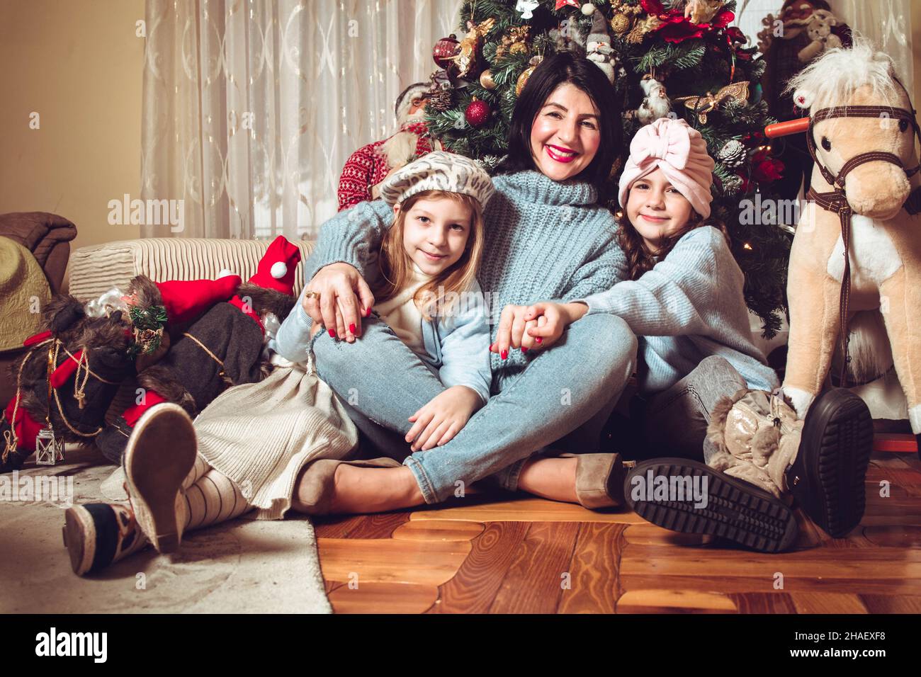 Mother and daughters sitting by the Christmas tree. Family holiday time Stock Photo