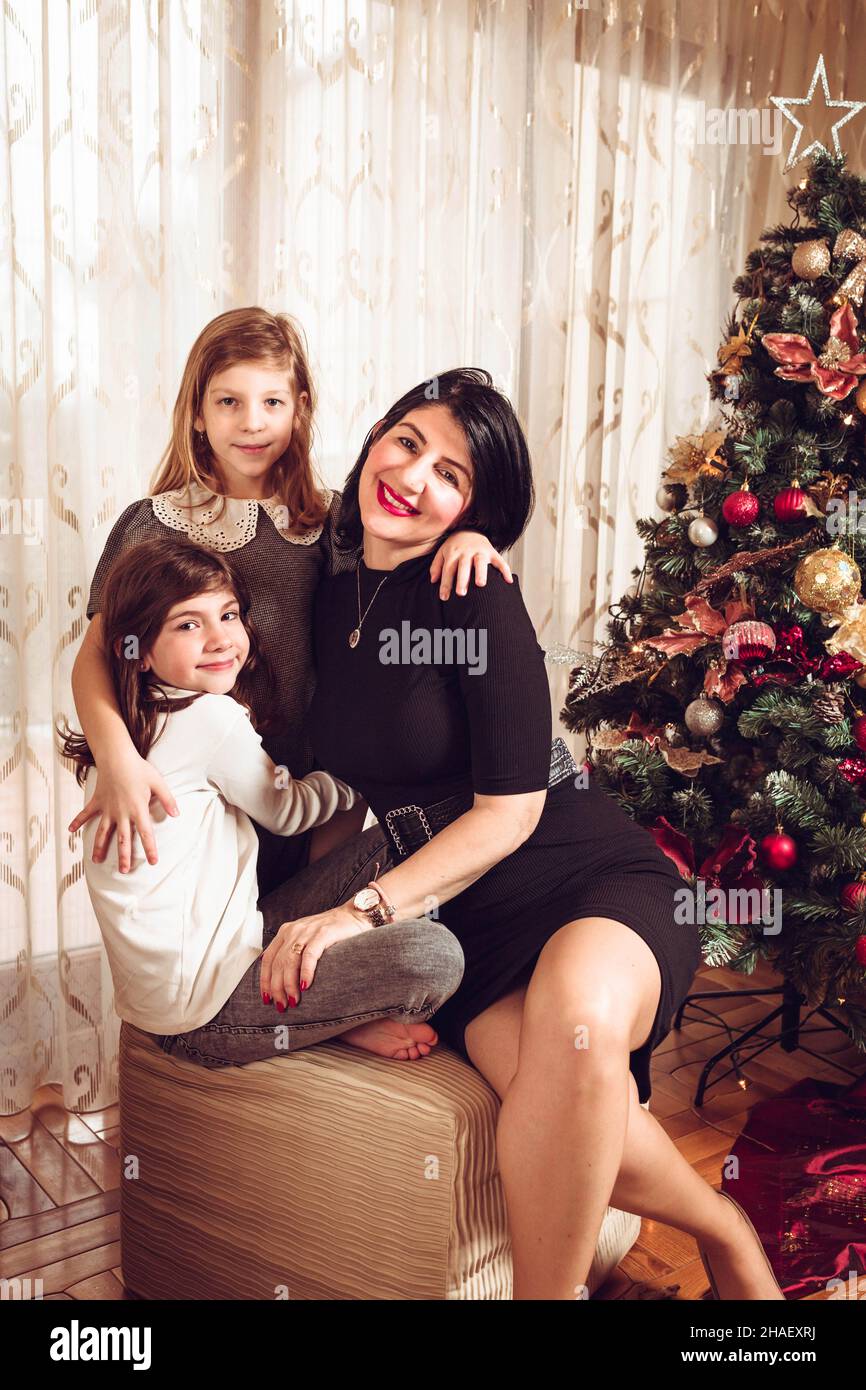 Mother and daughters sitting and hugging by the Christmas tree. Family holiday time Stock Photo
