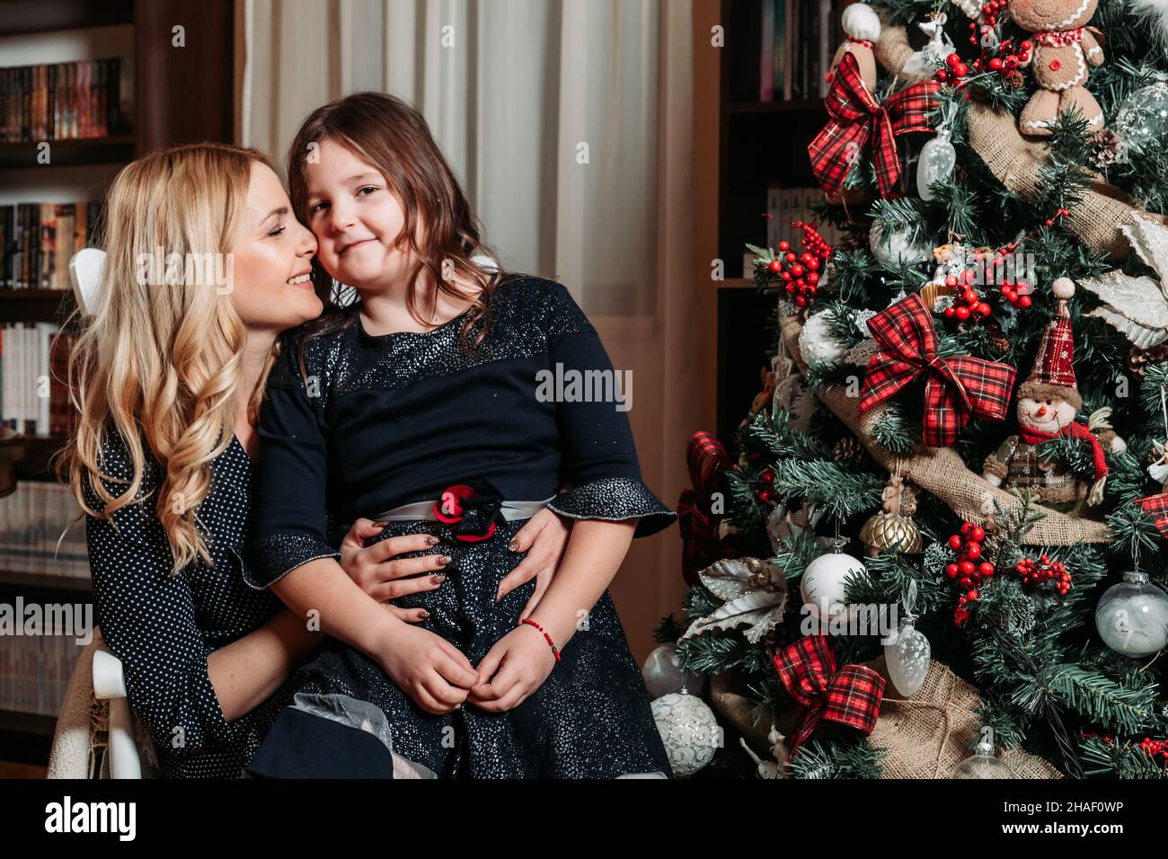 Mother and daughter sitting by the Christmas tree. Family holiday time Stock Photo