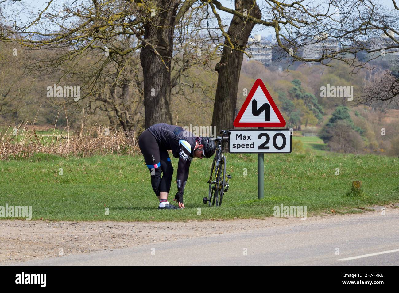London, England - April 17 2018: Male cyclist stretching next to a speed sign in Richmond Park, London Stock Photo