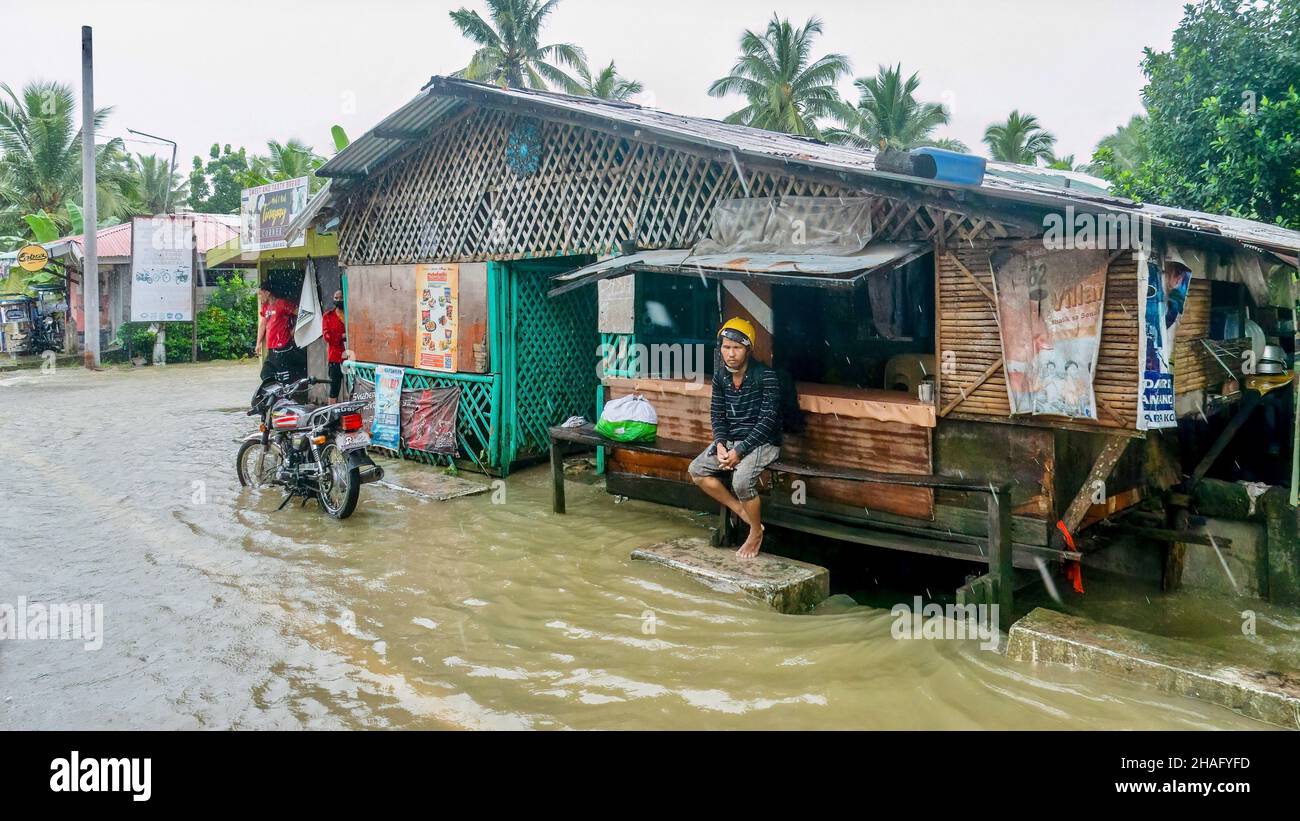 Baco, Oriental Mindoro, Philippines - July 23, 2021. Heavy monsoon rain flood a local restaurant along the National Highway, where a Filipino man sits Stock Photo
