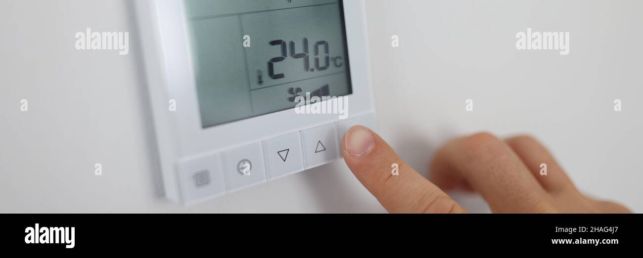 Person regulates air temperature in room through remote control on wall Stock Photo