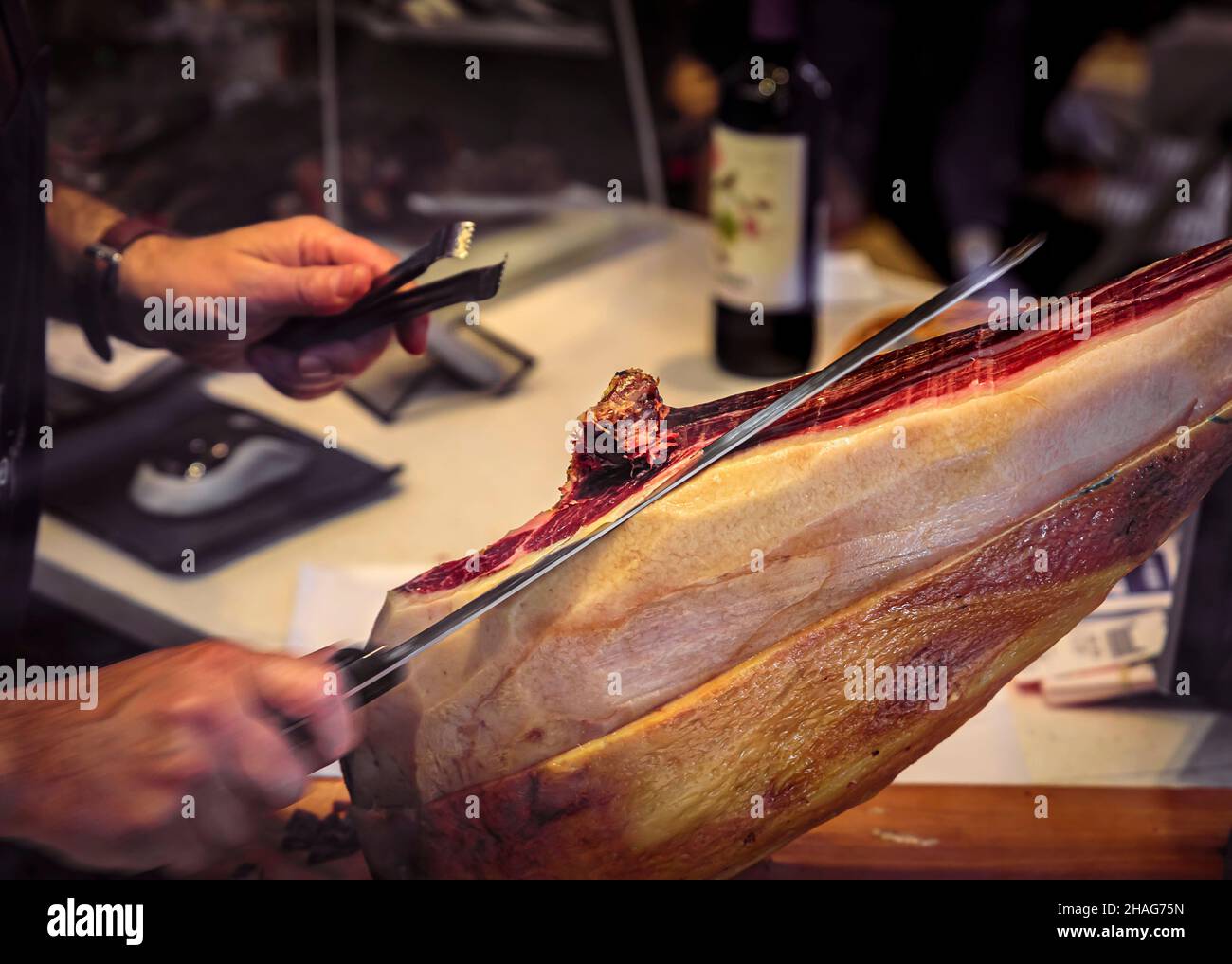 Whole bone-in leg of Spanish serrano iberico ham being carved at a local butcher shop in a restaurant, San Sebastian Donostia, Basque Country, Spain Stock Photo