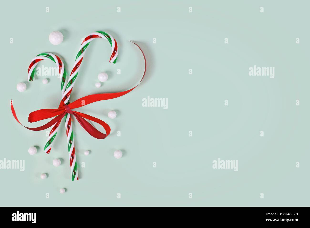 Two striped candy canes tied together with red ribbon on side of mint green background with copy space Stock Photo