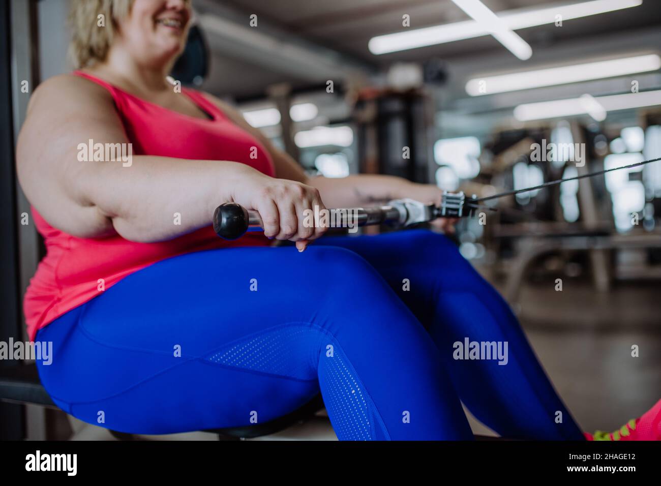 Unrecognizable plus size woman training on rowing machine machine indoors in gym Stock Photo