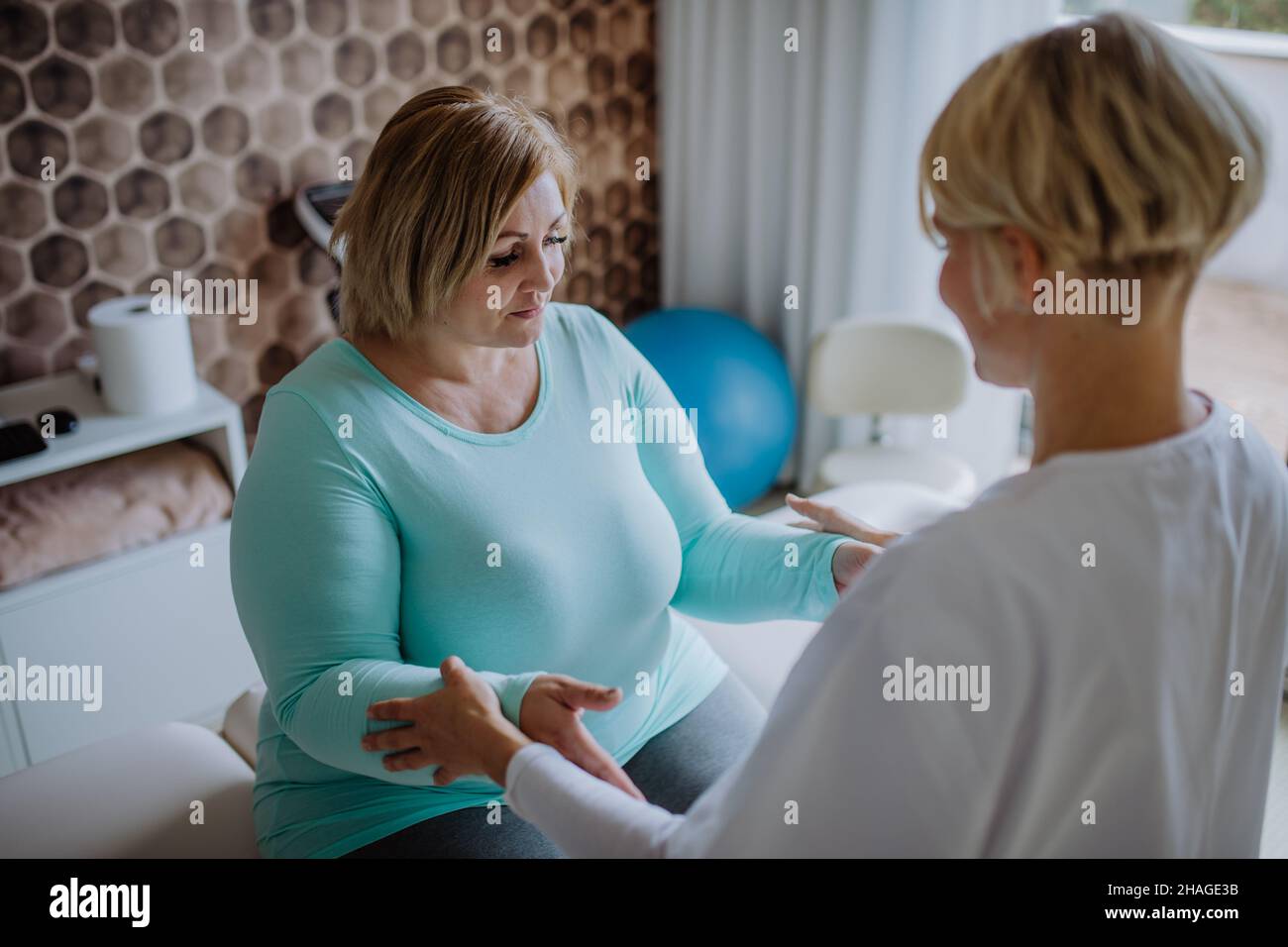 Mid adult physiotherapist woman exercising with overweight woman indoors in rehabilitation center Stock Photo