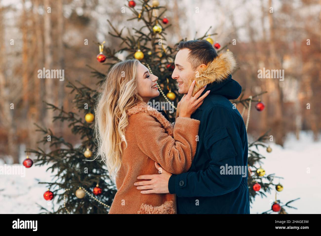 Young adult couple decorates christmas tree in winter forest. New year pine holiday party celebration concept Stock Photo