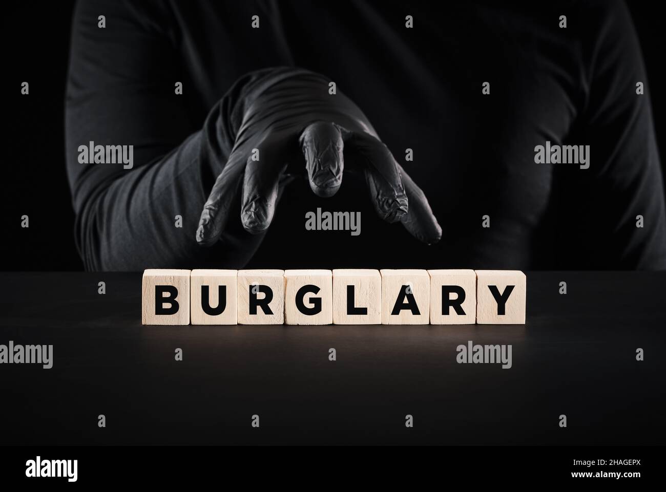 Theft, crime, robbery or burglary concept. Thief hand with black gloves over the word burglary written on wooden blocks. Stock Photo