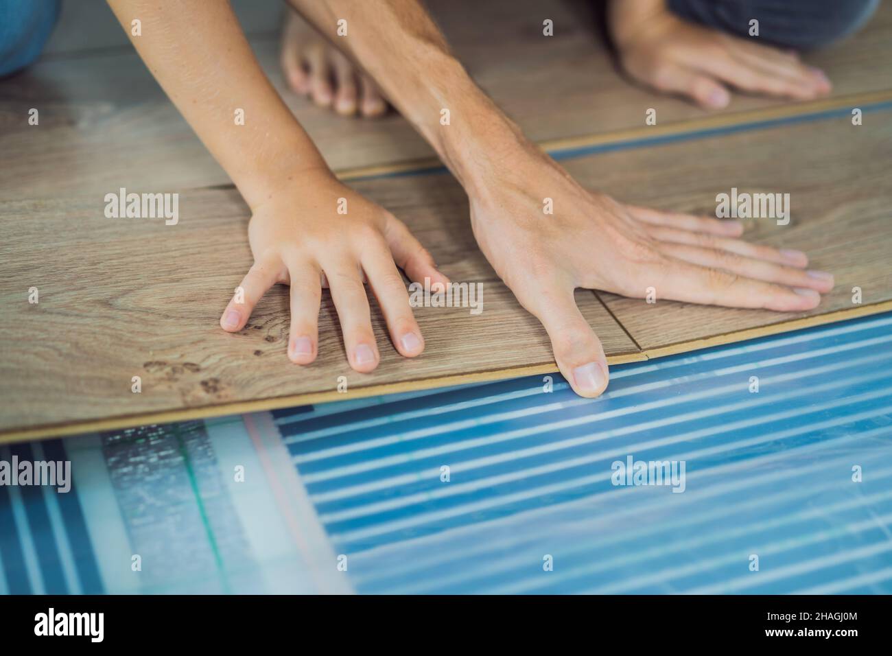 Father and son installing new wooden laminate flooring on a warm film floor. Infrared floor