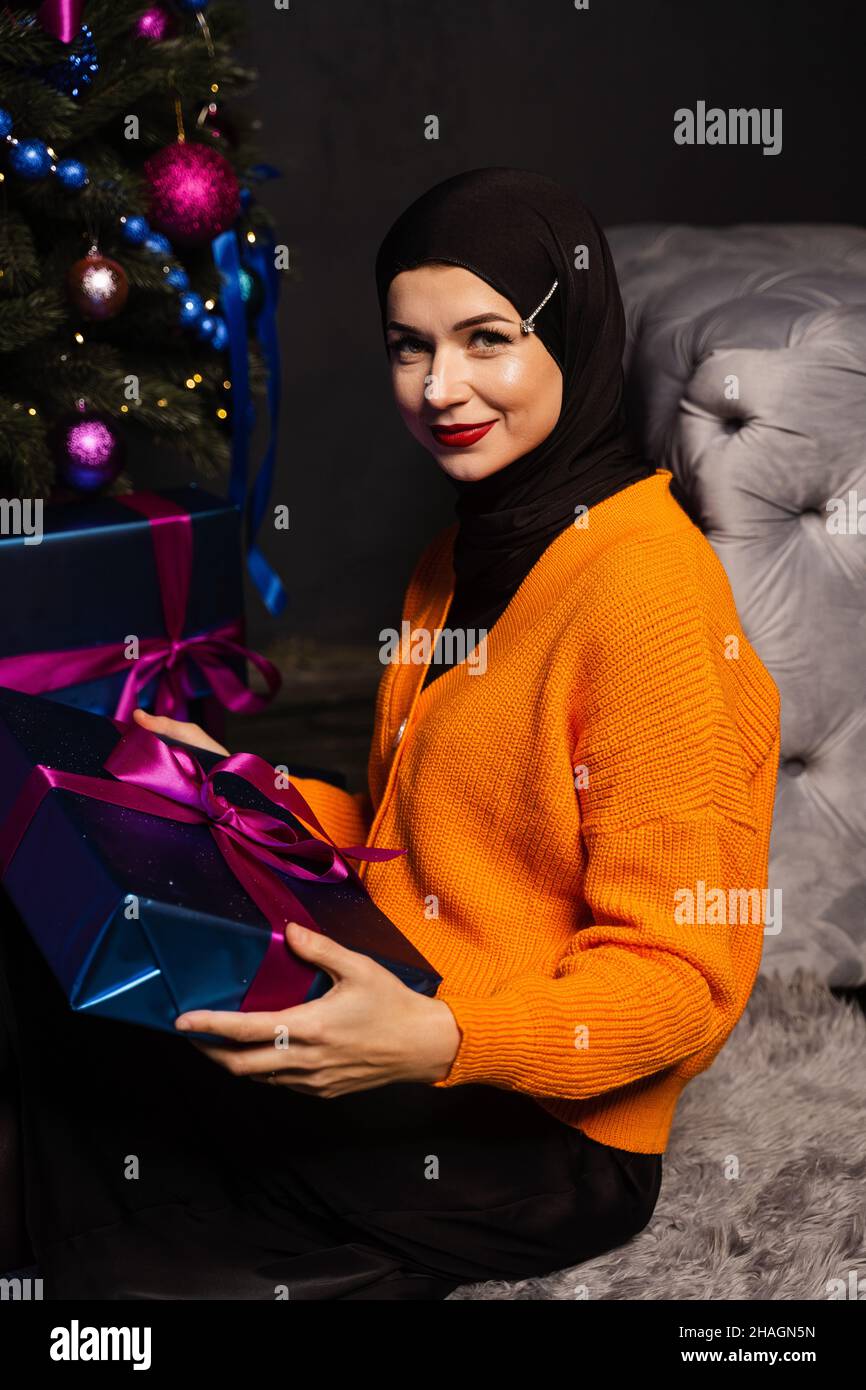 Muslim woman with gift near new year tree. Christmas celebration of