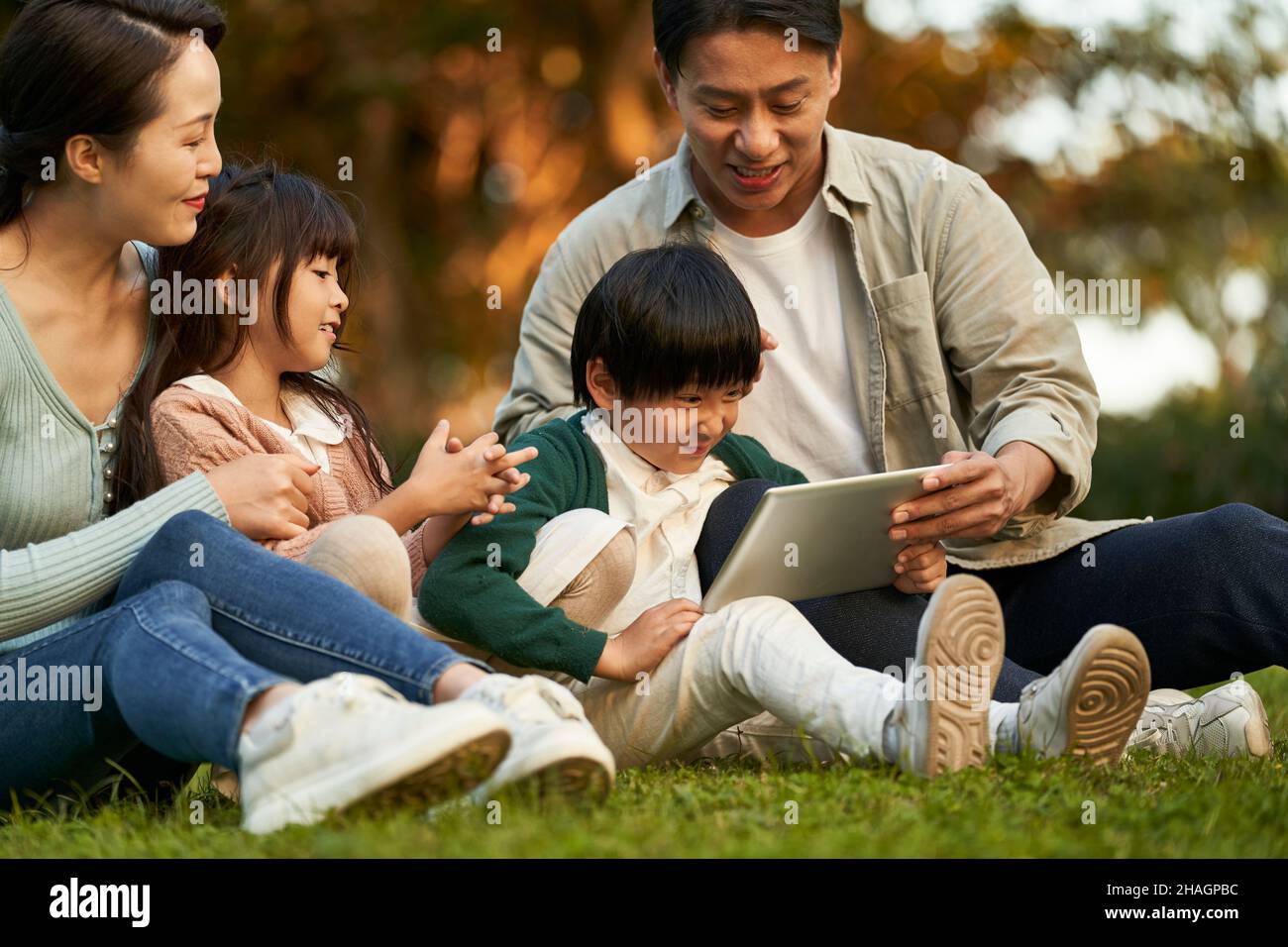 happy asian family with two children having a good time sitting on grass relaxing in city park at sunset Stock Photo