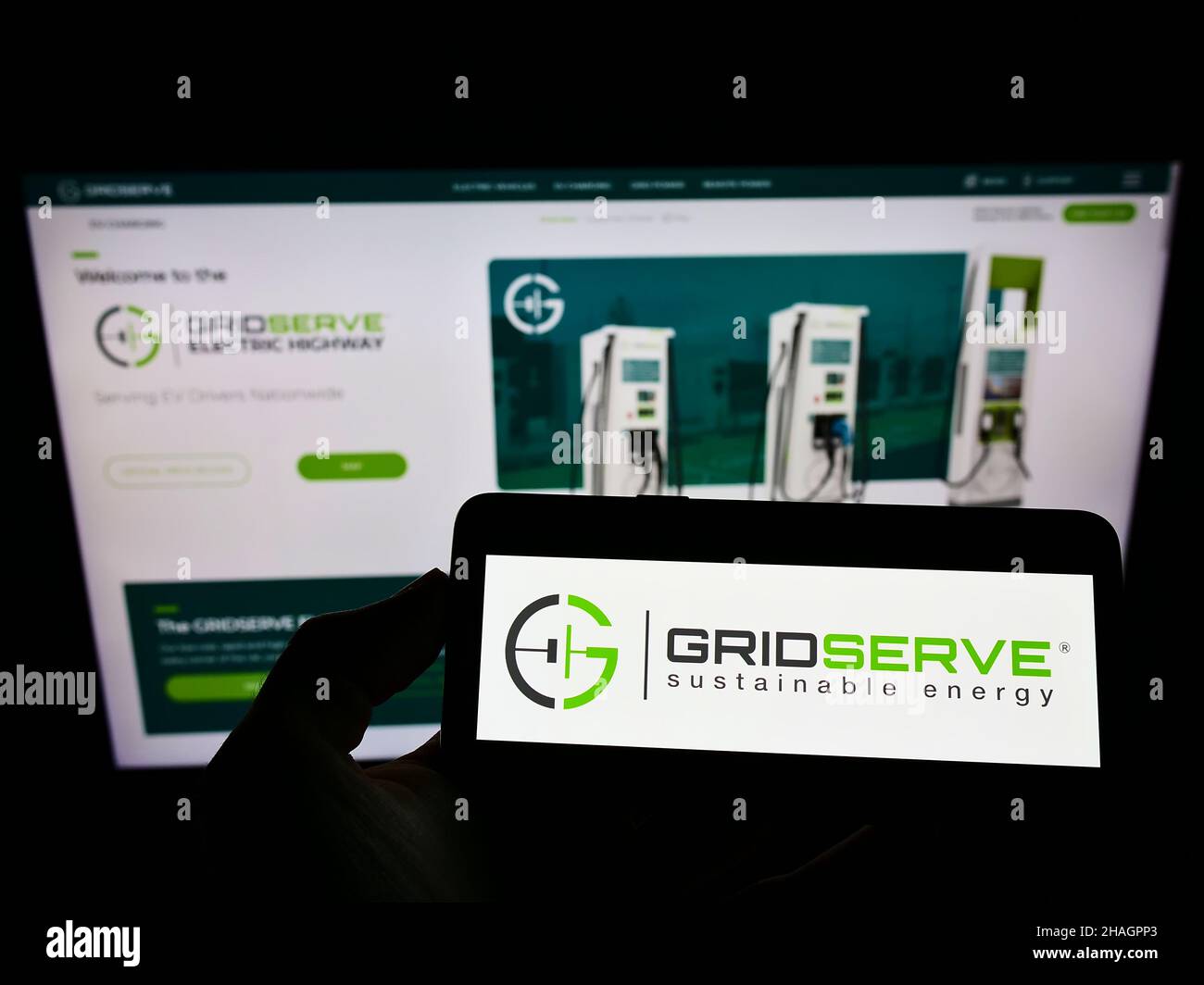 Person holding cellphone with logo of British company GRIDSERVE Sustainable Energy Limited on screen in front of webpage. Focus on phone display. Stock Photo