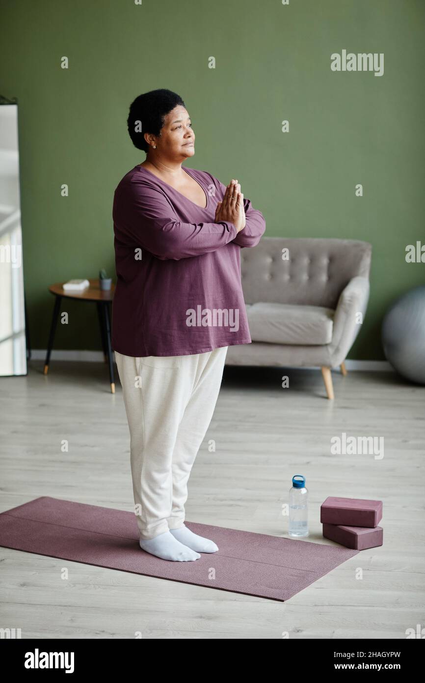 Vertical full length portrait of black senior woman meditating at home ...