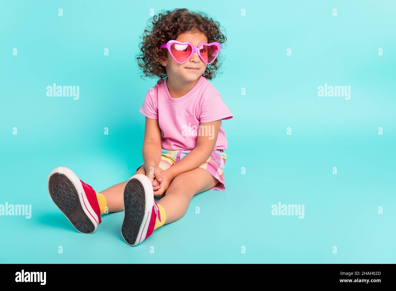 Portrait of attractive cheerful girl wearing big pink specs sitting resting isolated over bright teal turquoise color background. Stock Photo