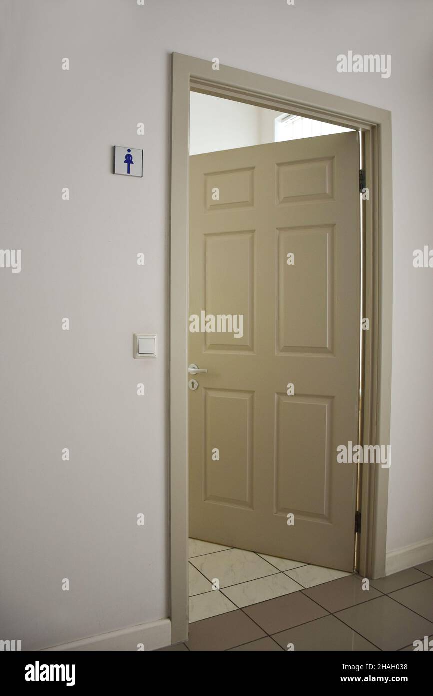 A light-colored open door to the women's toilet with a sign on the wall. The floor is covered with tiles. Frame in perspective Stock Photo