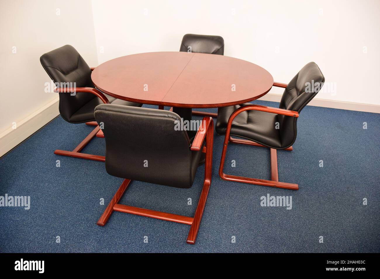 Four empty leather decorative office chairs sit around a brown round table. Stock Photo