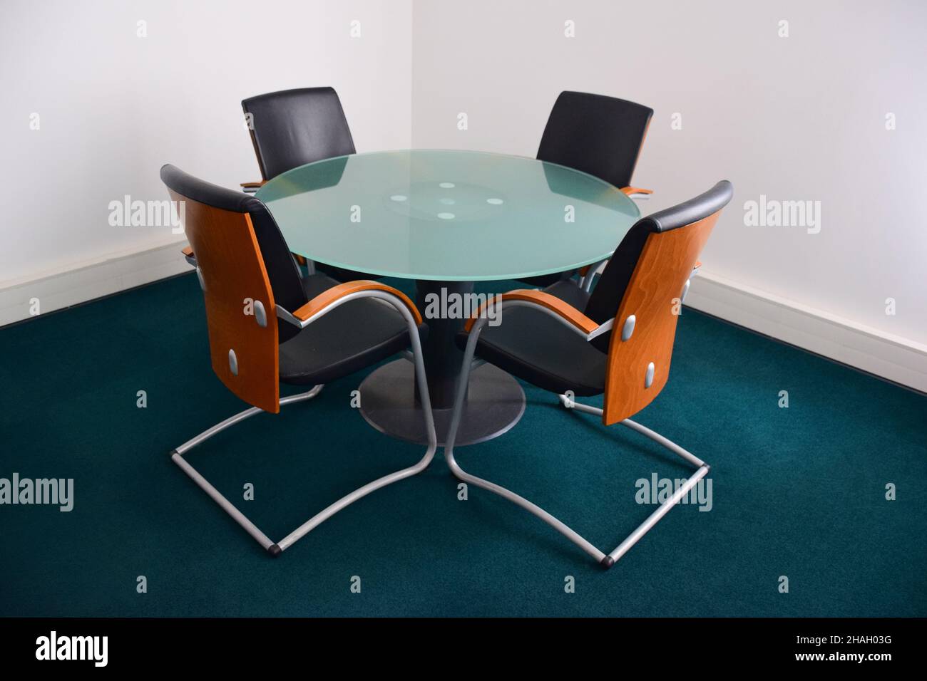 Four empty leather decorative office chairs with wooden backs sit around a glass circular table. Side view Stock Photo