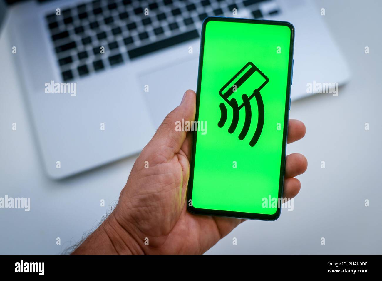 Close up view of hand with smartphone and contactless payment logo on display. Laptop on background. New technology, crypto value, wireless pay, conce Stock Photo