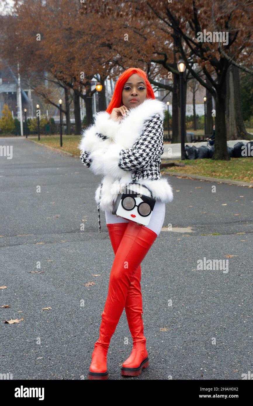 An attractive woman with long orange red hair and thigh high red boots. In a park in Queens, New York City. Stock Photo