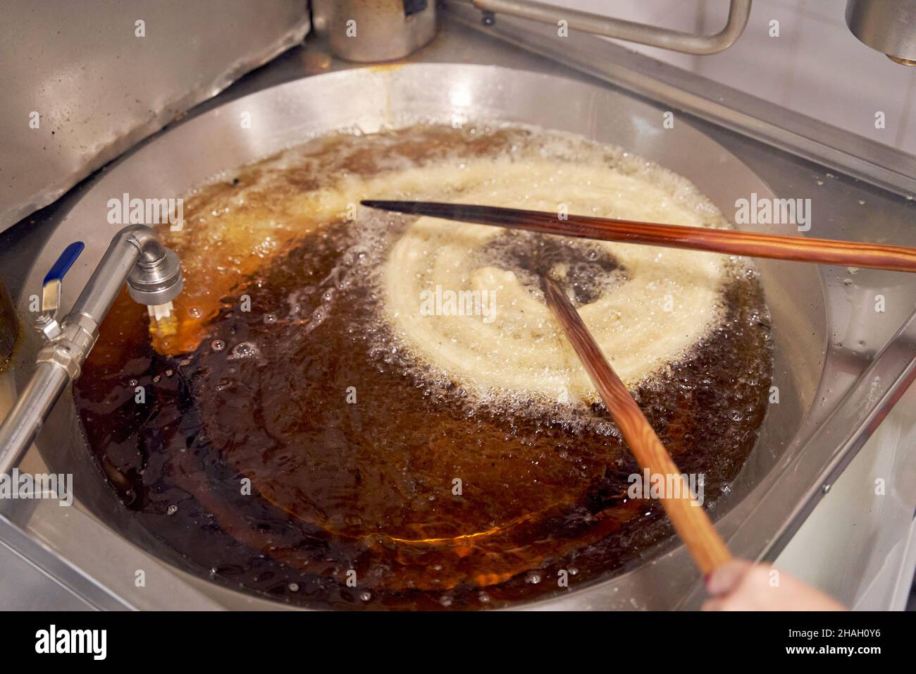 View from above of an anonymous cook moving raw dough with chopsticks in boiling oil to make churros. Typical Spanish breakfast Stock Photo