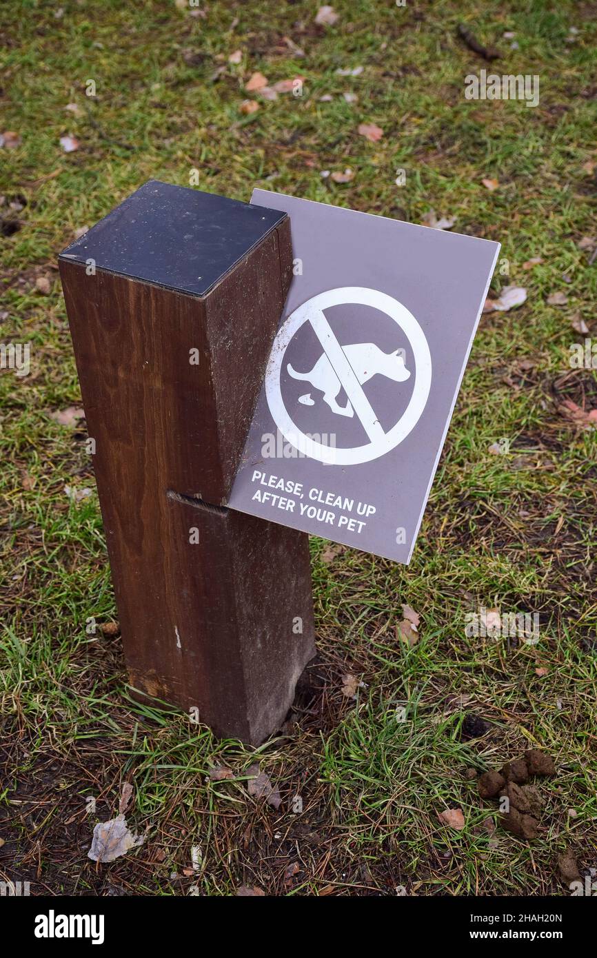 A post in the park encouraging dog owners to clean up excrement after their pets. Underneath is animal excrement Stock Photo