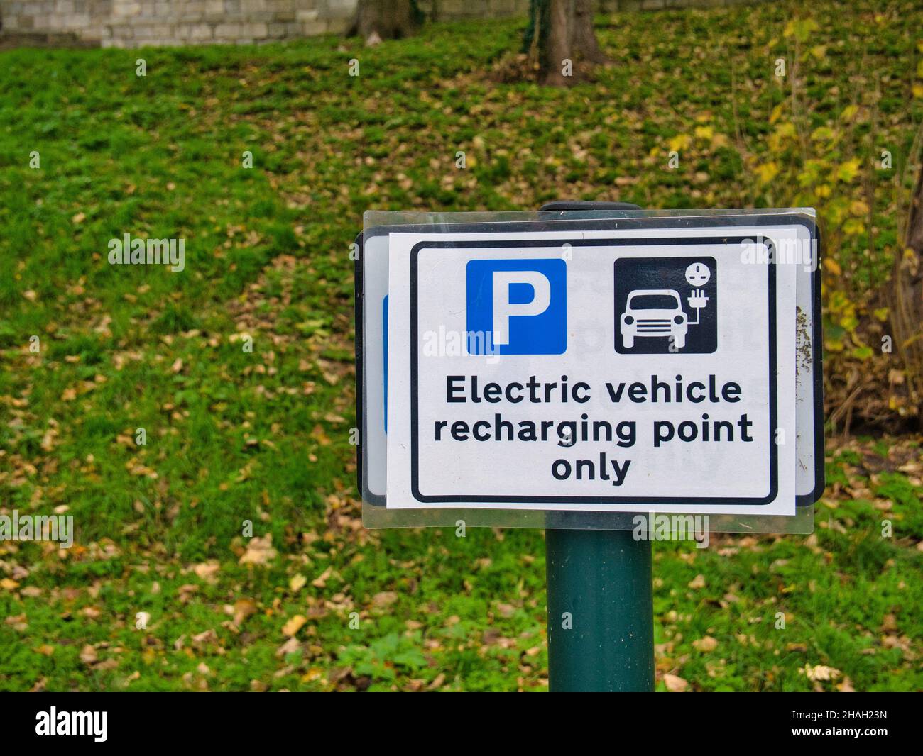A rectangular sign in a town car park shows a parking bay reserved for electric vehicle charging only. Stock Photo