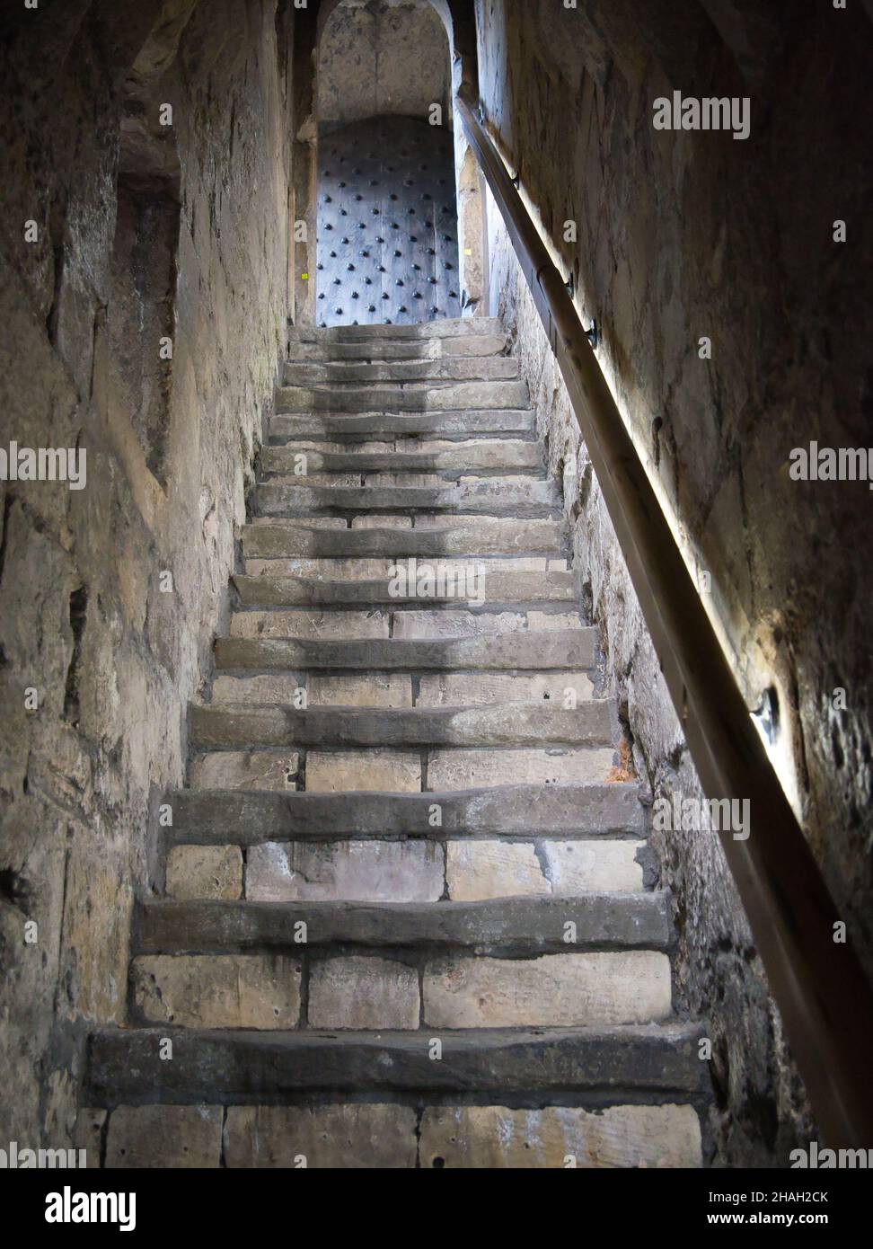 A steep flight of very old, stone steps between two stone walls leading to a studded wooden door. A handrail runs the length of the stairs. Stock Photo