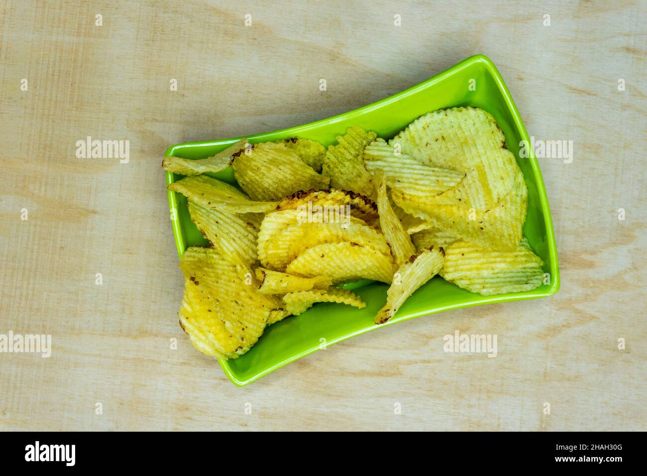 Salted Potato Wafers in Green Square Bowl on Wooden Table, Heap of Wafers, Copy Space, Heap of Chips, Top View Stock Photo