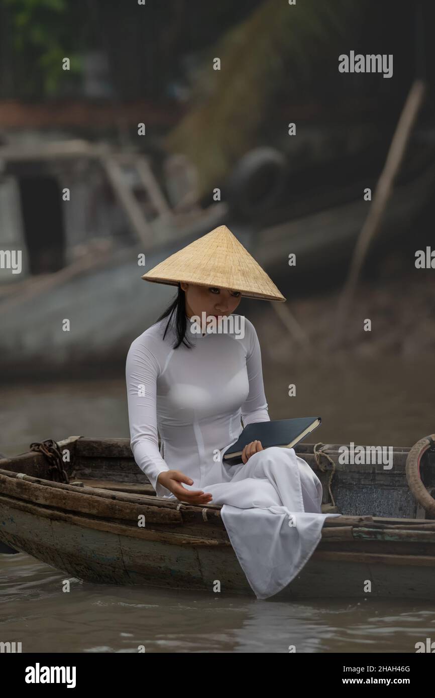 Can Tho, Vietnam-April 7, 2018: Traditionally dressed young Vietnamese woman takes a boat tour with an old boat woman on Mekong River Stock Photo