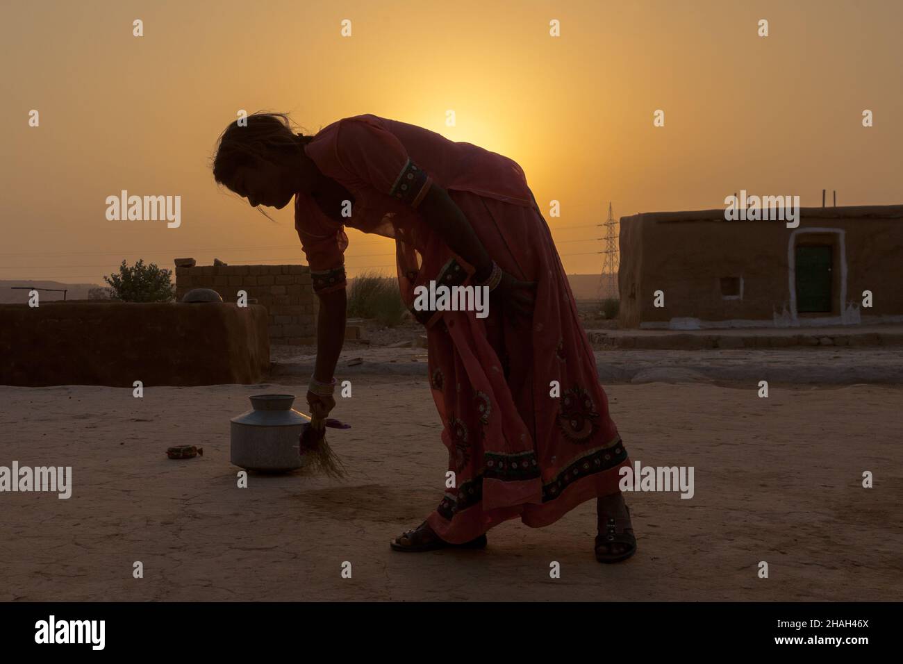 young woman sweeps in front of her house in her village during sunrise Stock Photo
