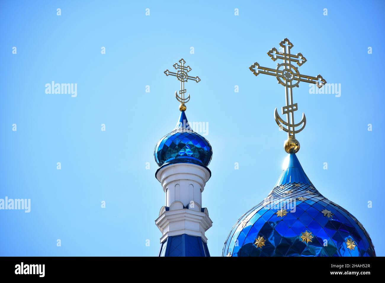 Against the background of a clear blue sky, two domes of a Christian church or monastery of different sizes, with crosses at the top Stock Photo