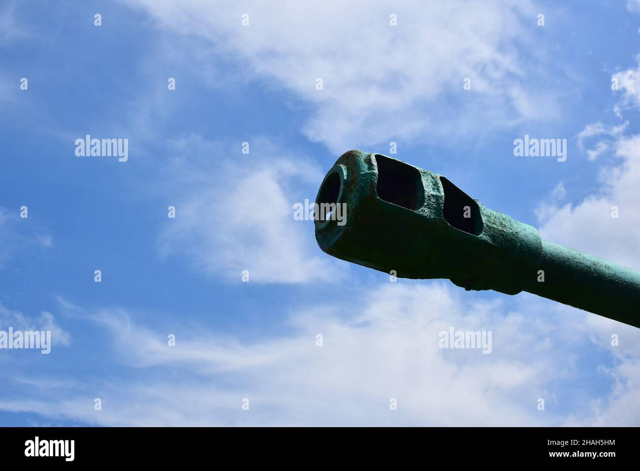 On the right side of the frame, the muzzle of a tank or cannon is turned into a bright blue sky. On the left side there is an empty space for an inscr Stock Photo