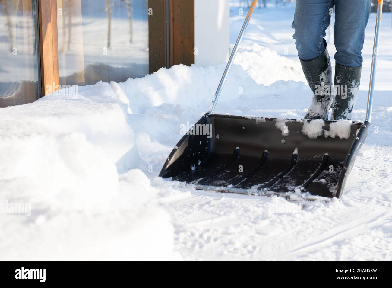 a man in rubber boots with a snow shovel cleans the snow from the ...