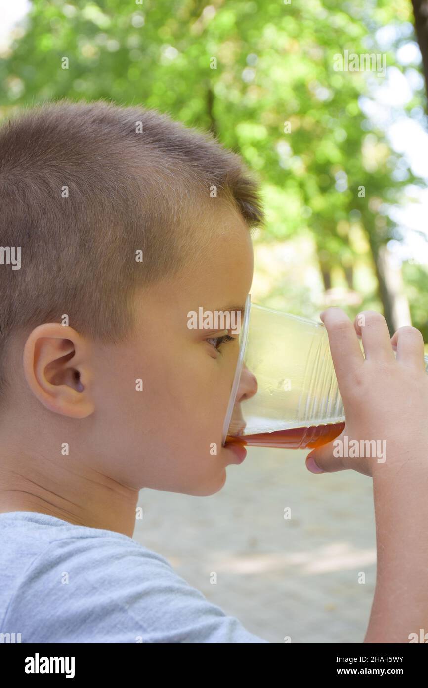 Little boy drinks from a large plastic clear glass of lemonade close up. Shot from the side. The background is blurred Stock Photo