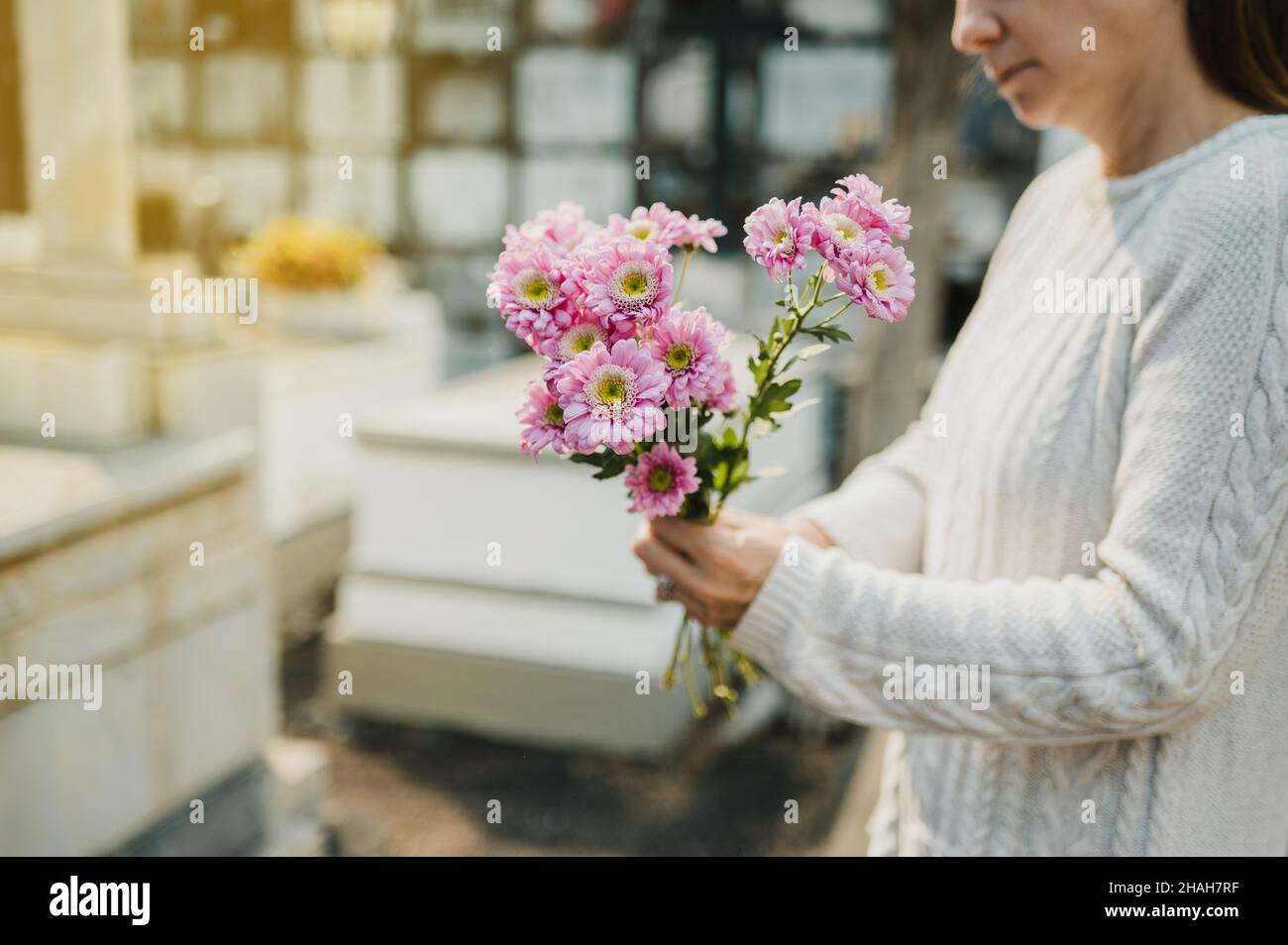 Crop woman with flowers in hands standing near gravestone in cemetery Stock Photo