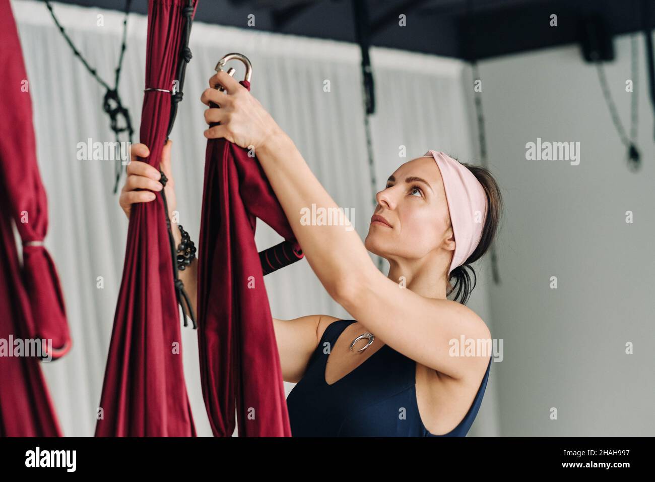 A woman fastens a hook from a hanging hammock for yoga in the gym. Stock Photo
