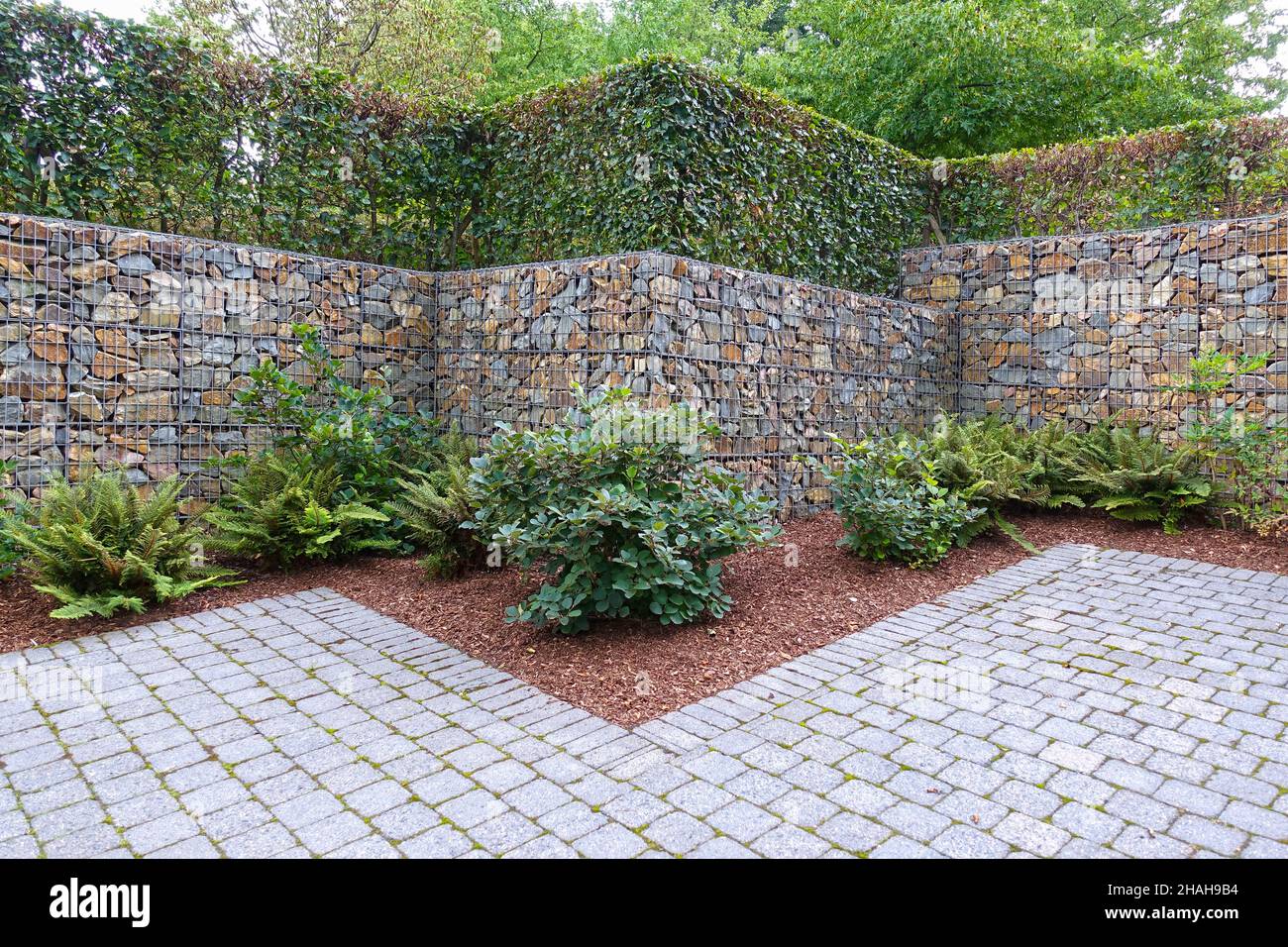 Modern enclosure made of a natural stone or gabion fence, hedge and cobblestone pavement. Stock Photo