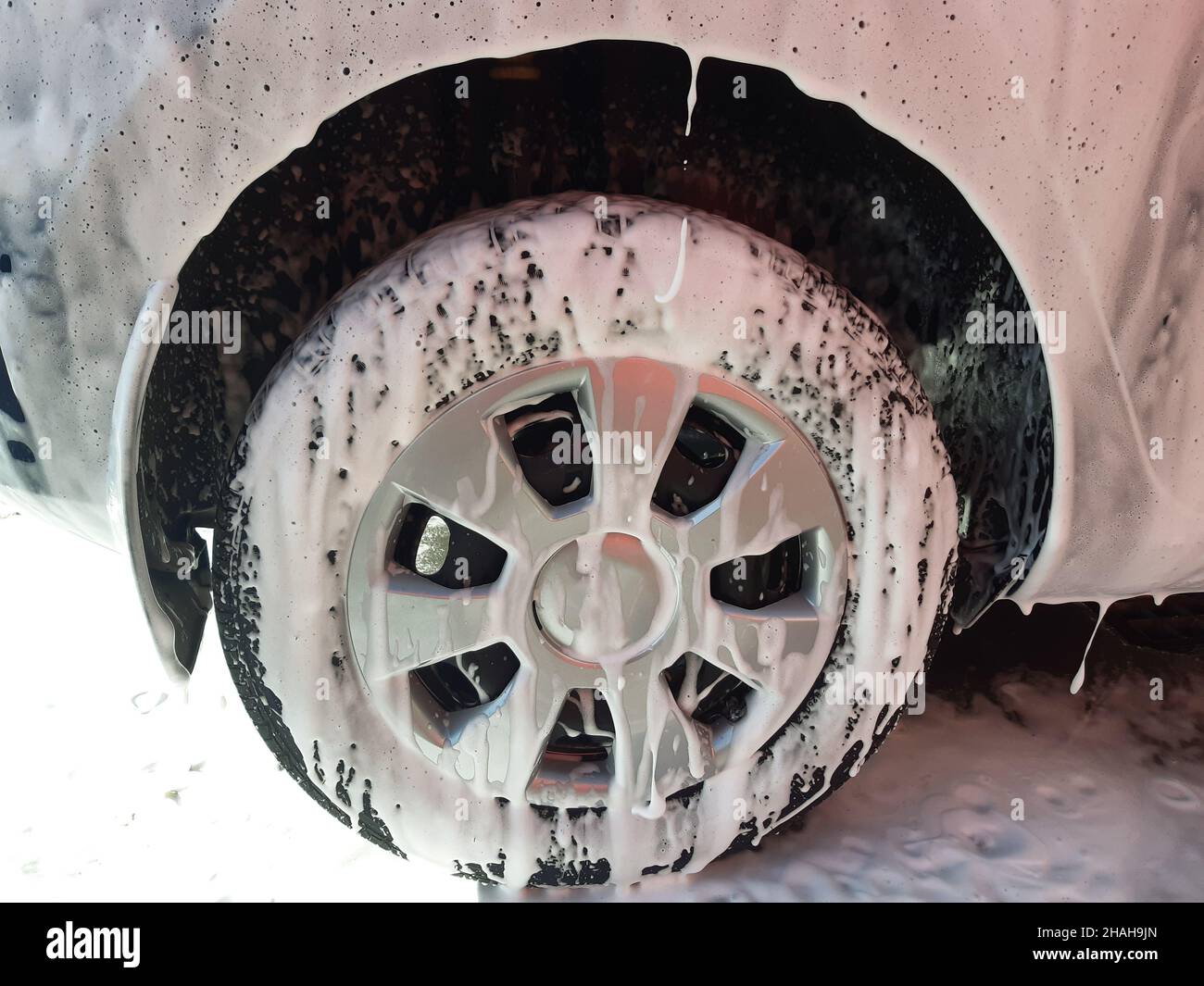 The wheel of the car and part of the fender of the car are all completely covered in white foam at the car wash prepared for washing off with water. F Stock Photo