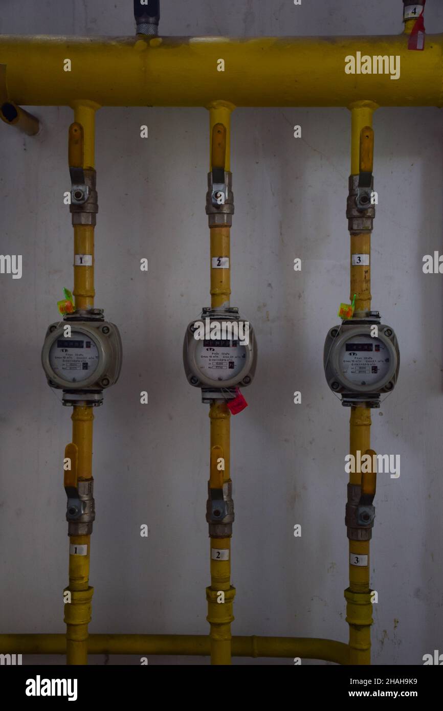 Several gas meters in a row with yellow iron pipes emanating from them and switches Stock Photo