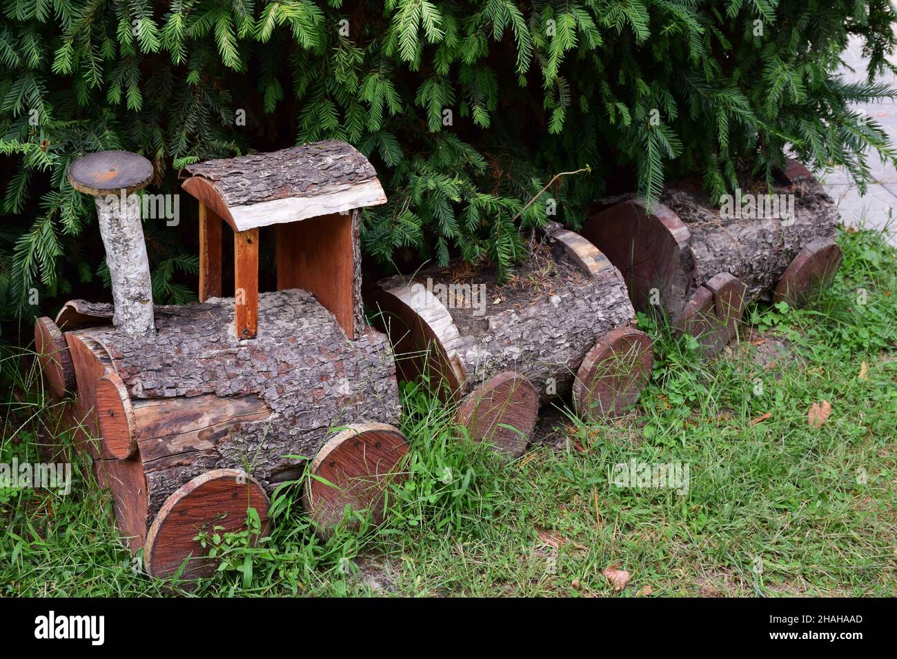 A small decorative locomotive and two carriages made of logs stand under a spruce for fun for children and tourists Stock Photo