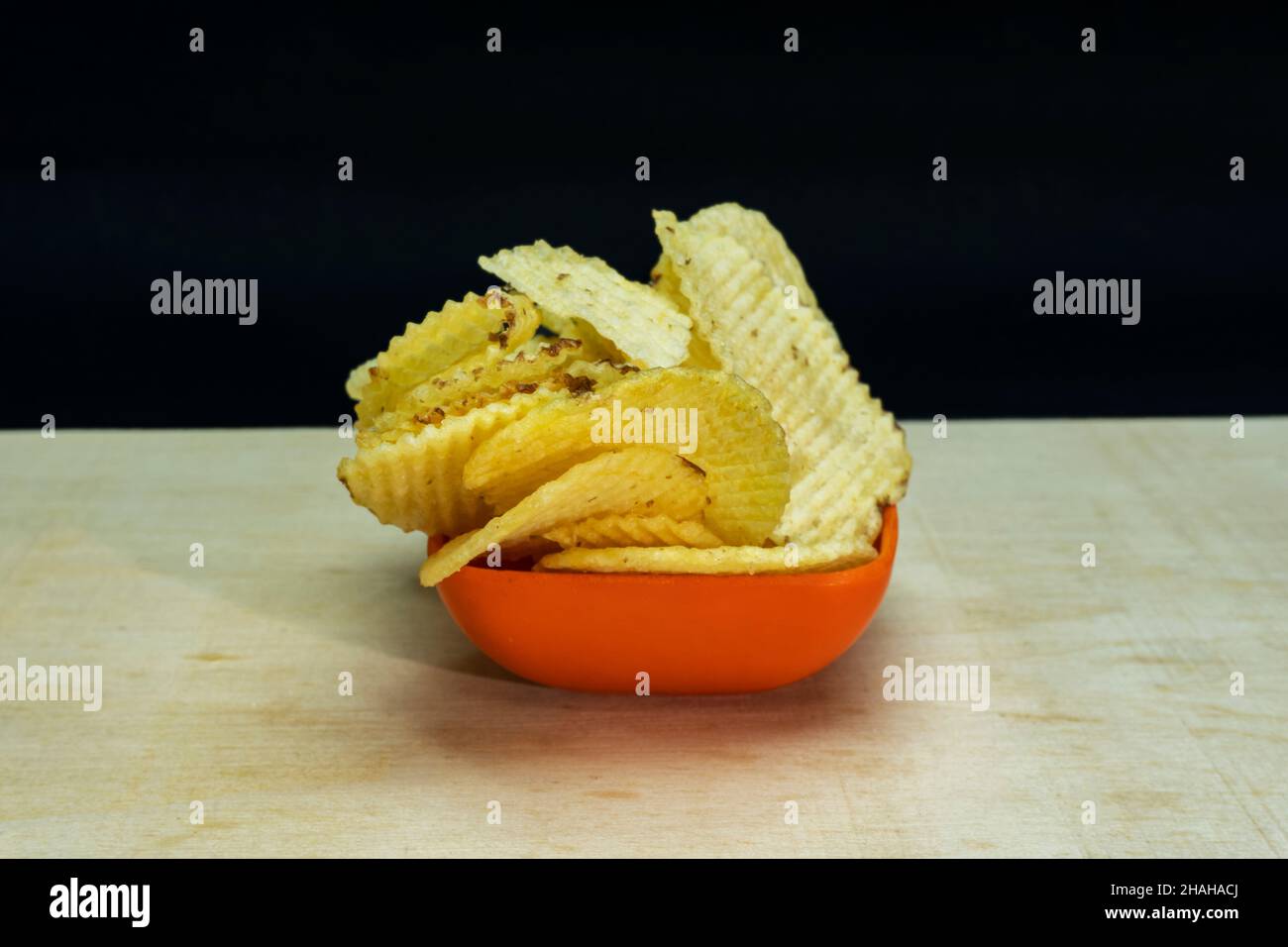 Salted Potato Wafers in Small Saffron Square Bowl On Wooden Table, Heap of Wafers, Copy Space, Heap of Chips, Side View Stock Photo