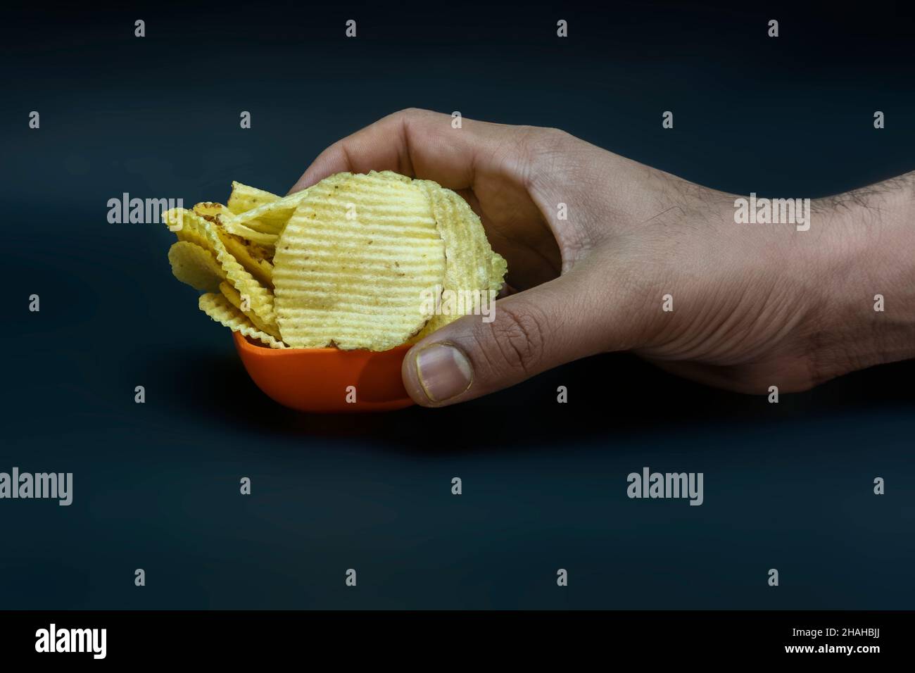 Salted Potato Wafers in Small Saffron Square Bowl With Hand, Heap of Wafers, Copy Space, Heap of Chips, Side View Stock Photo