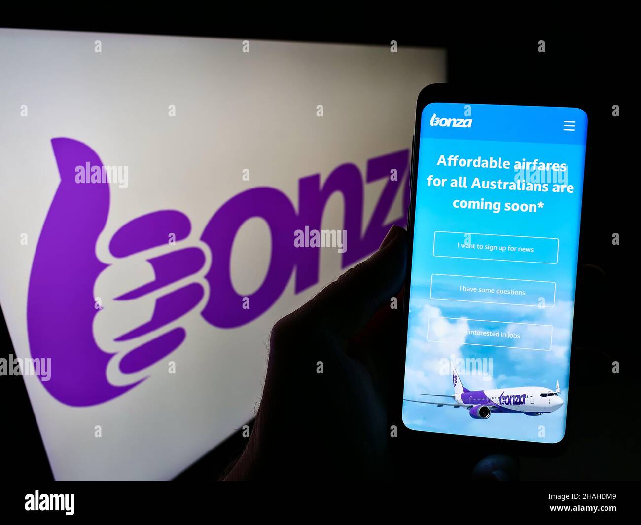 Person holding mobile phone with website of Australian airline Bonza Aviation Pty Ltd. on screen in front of logo. Focus on center of phone display. Stock Photo