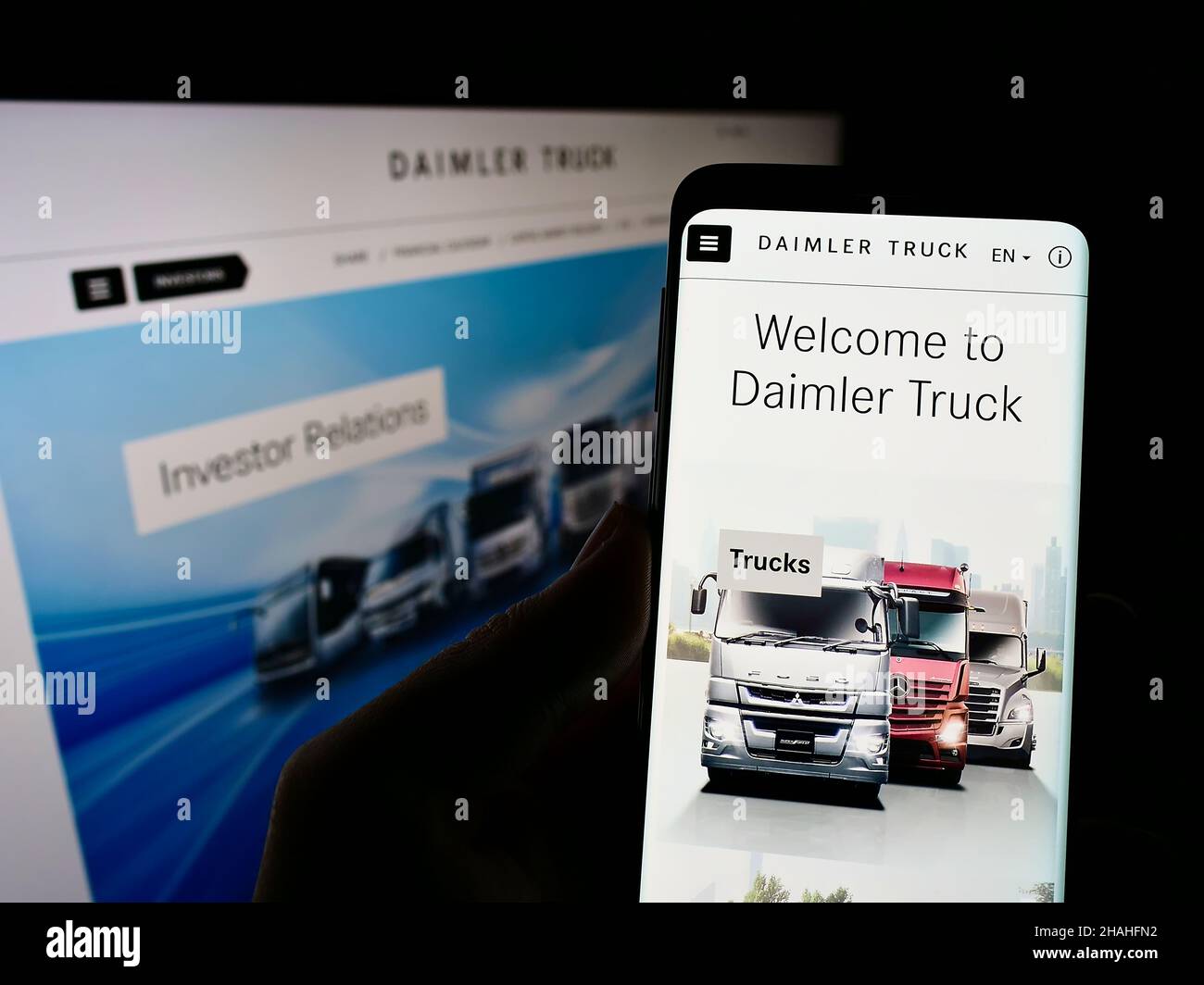 Person holding smartphone with website and logo of German commercial vehicle manufacturer Daimler Truck AG on screen. Focus on center of phone. Stock Photo