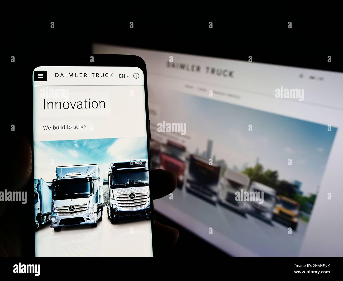 Person holding cellphone with website and logo of German commercial vehicle manufacturer Daimler Truck AG on screen. Focus on center of phone. Stock Photo