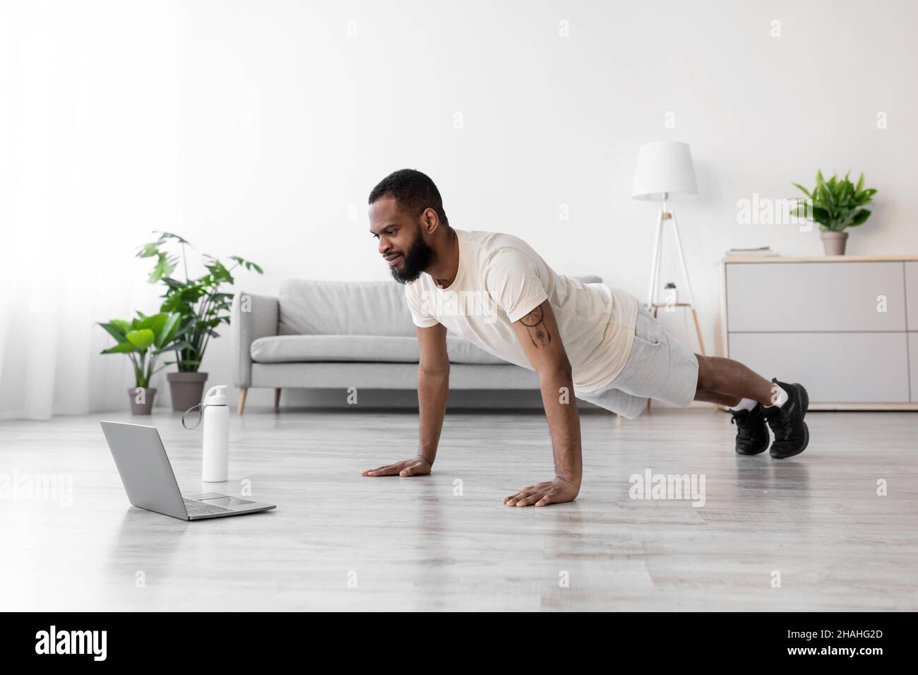 Attractive serious young african american man with beard in white sportswear in minimalist living room Stock Photo