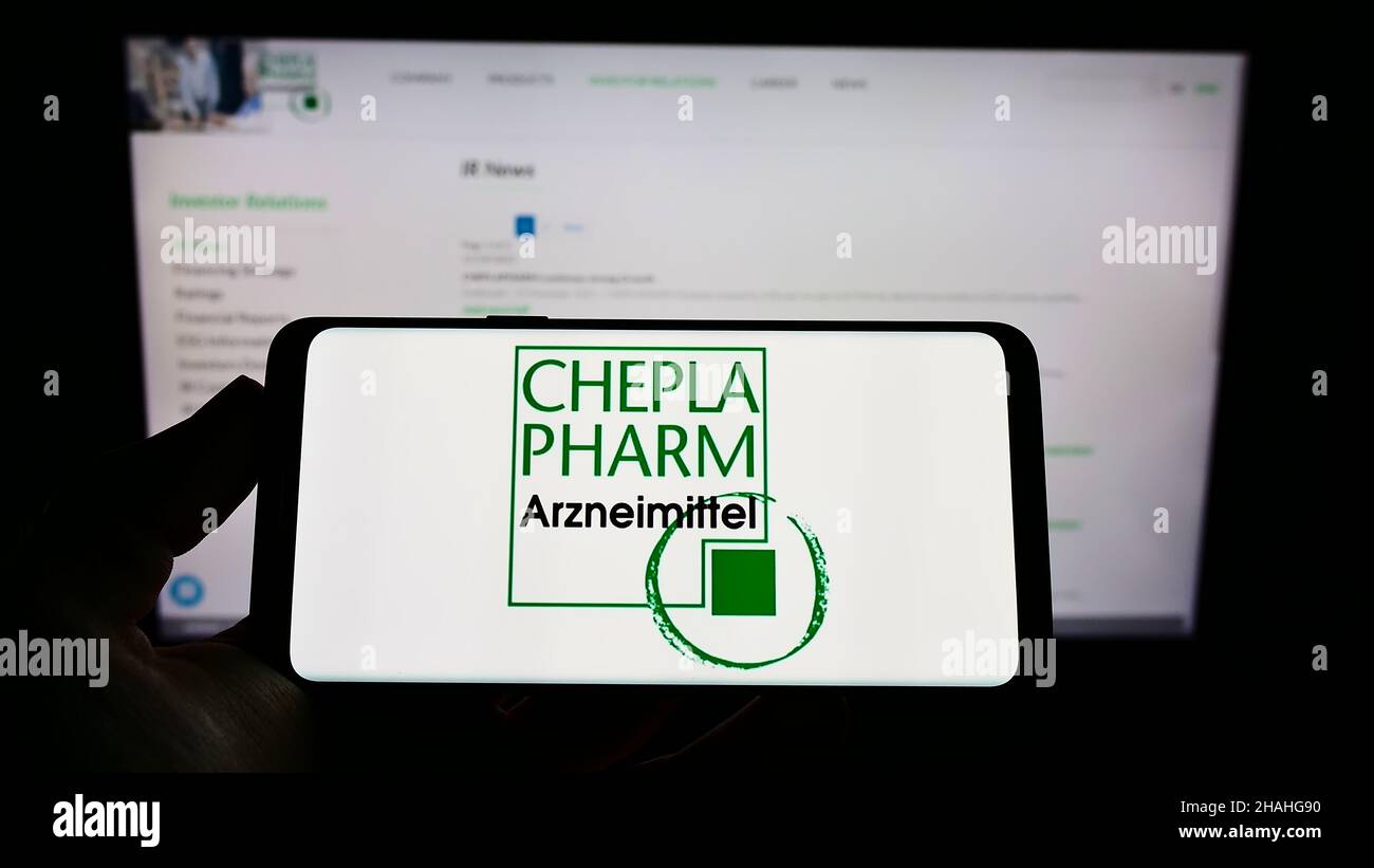 Person holding cellphone with logo of German pharma company Cheplapharm Arzneimittel GmbH on screen in front of webpage. Focus on phone display. Stock Photo