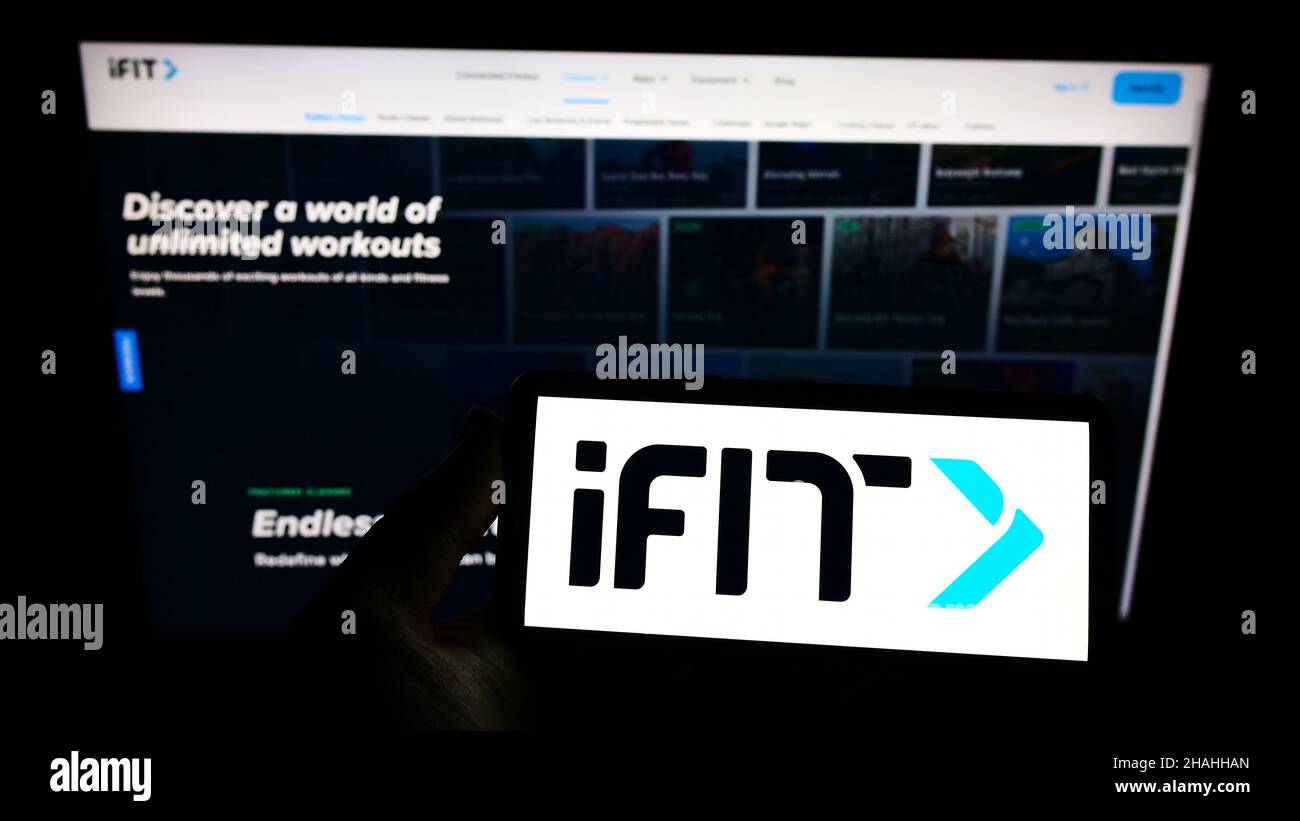 Person holding smartphone with logo of US fitness company iFIT Inc. on screen in front of website. Focus on phone display. Stock Photo