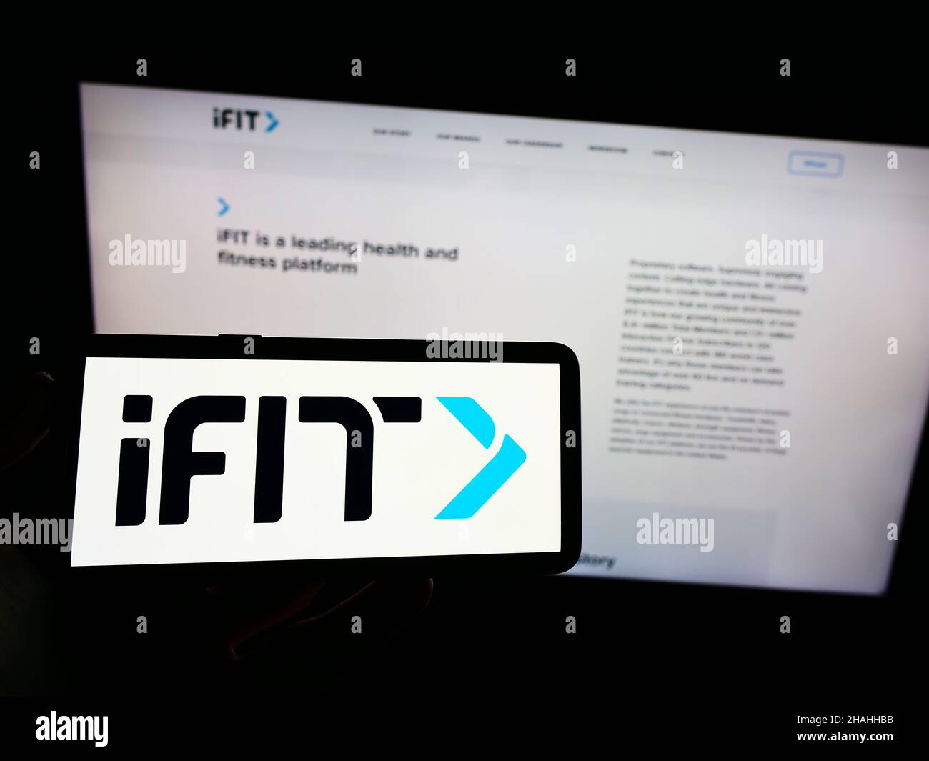 Person holding mobile phone with logo of American fitness company iFIT Inc. on screen in front of business web page. Focus on phone display. Stock Photo