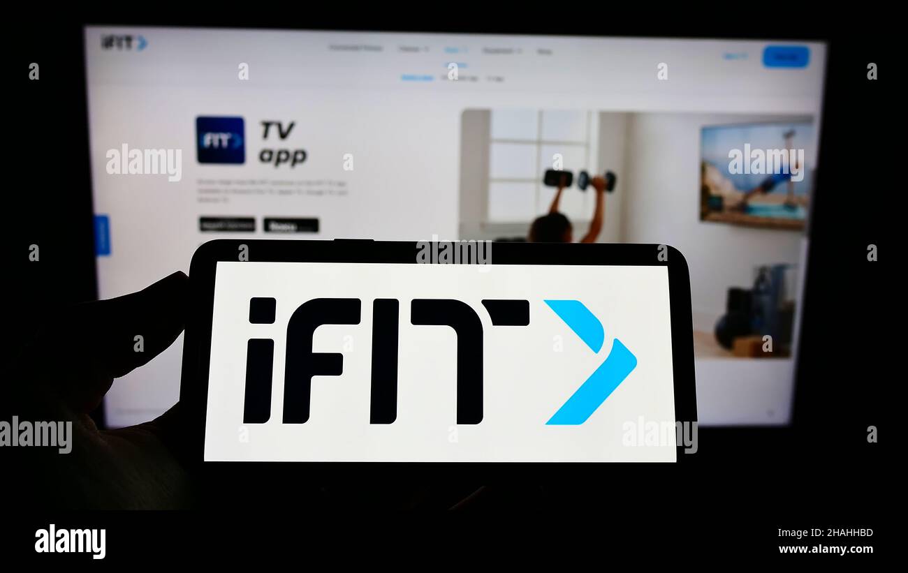 Person holding cellphone with logo of US fitness company iFIT Inc. on screen in front of business webpage. Focus on phone display. Stock Photo